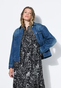 Jeansjacka i mörkblått med långa ärmar och knappstängning, bärs över en svart klänning med ett vitt himmelskt mönster.