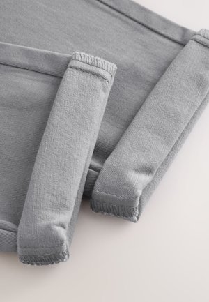 Nærbillede af foldede grå ærmer med ribbestrikkede manchetter og synlige syninger på en lys baggrund.