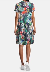 Kvinna som bär en knälång kortärmad klänning med ett livfullt blommigt mönster i flera färger, i kombination med vita sneakers, sedd bakifrån.