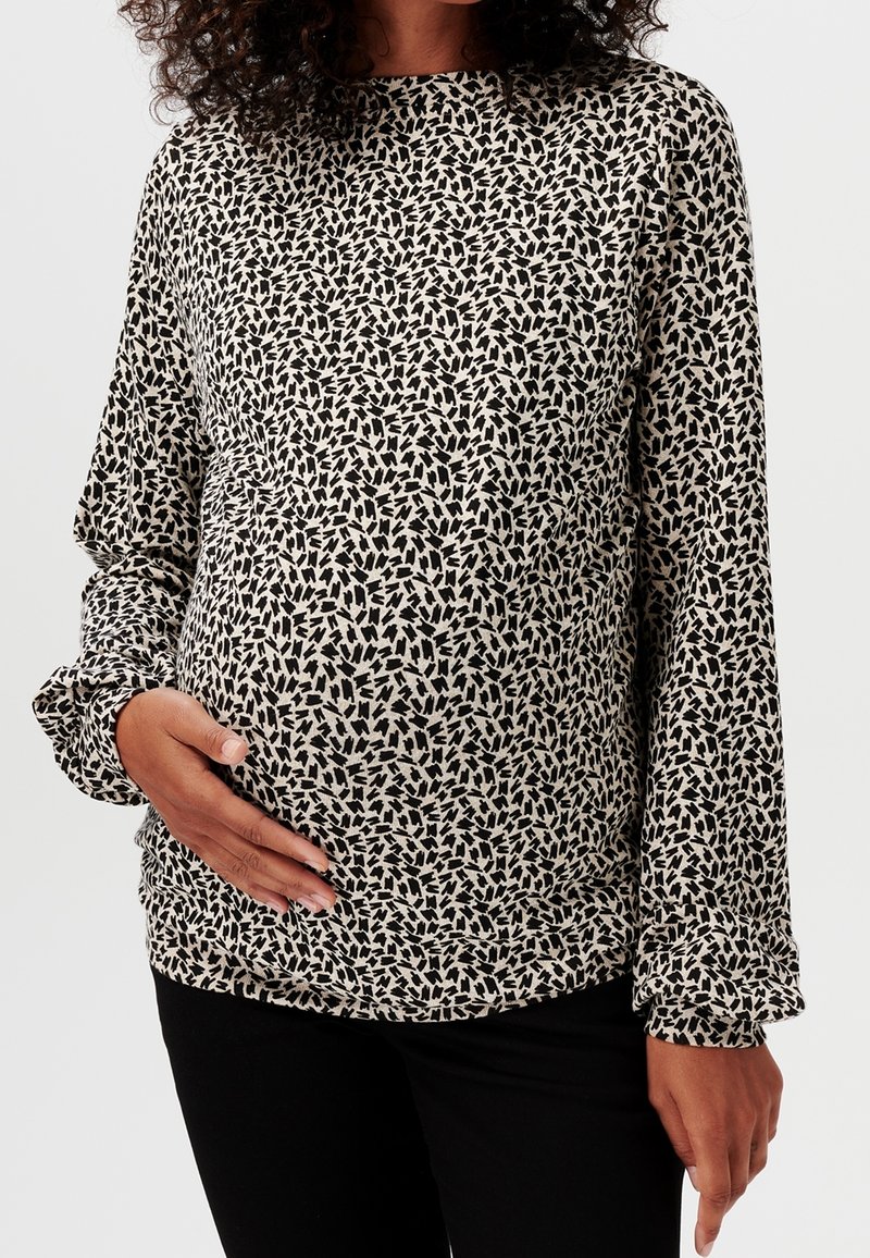 Maglietta premaman a maniche lunghe di colore beige con un motivo a foglie nere, con una vestibilità rilassata e polsini arricciati. Tessuto morbido ed elastico per il massimo comfort.