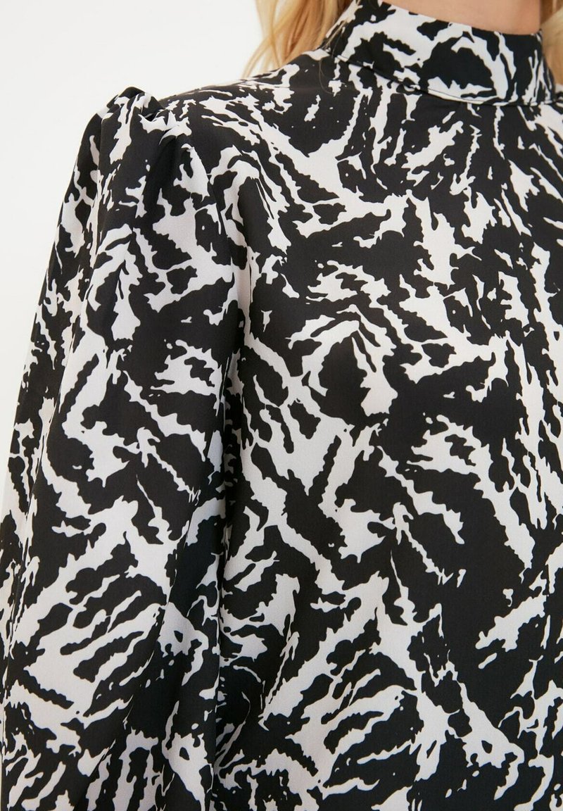 Czarna i biała bluzka w wzory z wysokim kołnierzem, wykonana z textured tkaniny i z bufiastymi rękawami. Odważny, abstrakcyjny wzór.