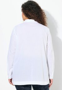 Witte lange mouwen blouse met een relaxte pasvorm, knoopsluiting bij de mouwen en een afgeronde zoom. Glad materiaal met een scherpe afwerking, minimale details op de achterkant.