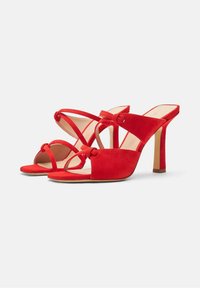 Sandales à talons hauts en suède rouge avec un design à lanières, présentant des détails entrelacés et une ouverture à l'orteil, reposant sur un talon fin.