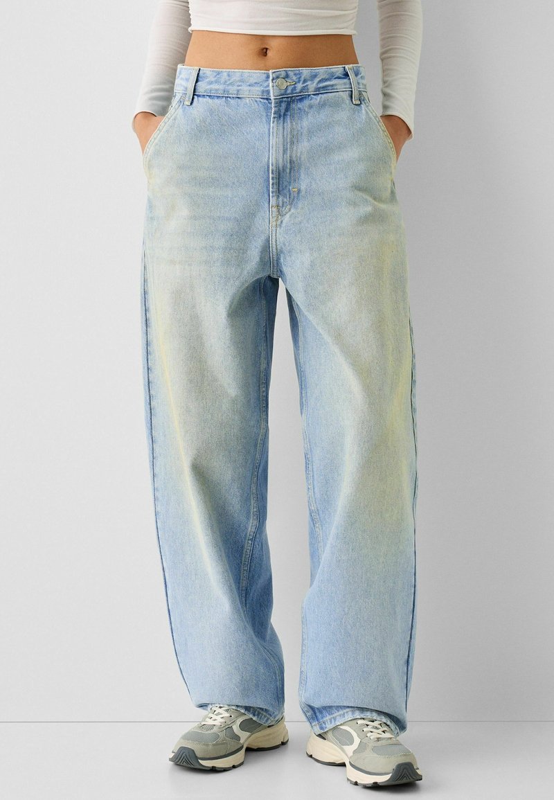 Light blue denim wide-leg jeans with a high waist, featuring side pockets and a faded texture. Paired with gray sneakers.
