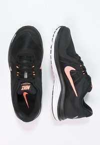 Black athletic shoes with mesh upper, pink accents, cushioned midsole, and rubber outsole. Features laces and Nike branding on tongue and side.