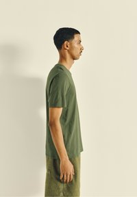 Olive-green short-sleeve t-shirt with a round neckline, slightly relaxed fit, worn with matching green textured shorts. Simple design.