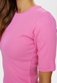 Gros plan sur une personne portant un haut rose à rayures ajusté à manches courtes, montrant l'épaule, le cou et une partie des cheveux.