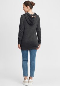 Kullsvart hettegenser med kengurulomme og en brun lærtag, akkompagnert av blå skinny jeans og beige sneakers.