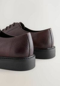 Des chaussures en cuir bordeaux foncé avec une finition texturée, un bout rond et une semelle en caoutchouc noir. Présentent des coutures discrètes et un design à lacets.