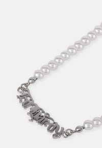 Colar de corrente de prata com pérolas brancas e um encantamento de metal estilizado intrincado. As pérolas são redondas e bem espaçadas.