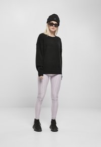 Fekete, túlméretezett pulóver, textúrált világoslila leggings négyzetrácsos mintával, és fekete fűzős bokacsizma, melyekhez fekete sapka és napszemüveg társul.