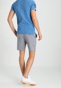 Modrá bavlněná polo tričko s krátkým rukávem a číselným detailem. Slučuje s šedými šortkami a bílými teniskami, ukazuje neformální, sportovní vzhled.