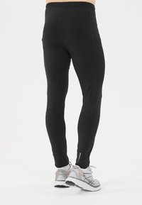 Zwarte sportleggings met een aansluitend ontwerp, gladde textuur en subtiele zijnaaddetail. Gecombineerd met lichtgrijze en oranje hardloopschoenen.