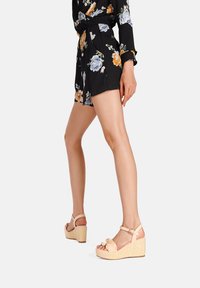 Sandali wedges beige con dettaglio annodato sul davanti e cinturino alla caviglia. Il wedge è realizzato in materiale testurizzato simile alla paglia, offrendo un aspetto leggero.