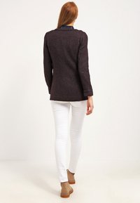 Tmavě fialové texturované sako s dlouhými rukávy, výstřihem do klínu a ohrnutými manžetami. Nosit ho přes bílé úzké džíny a tanové kotníkové boty.