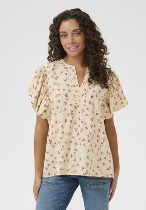 Blusa amarilla con estampado floral que presenta mangas cortas y fruncidas, un escote en forma de V y una tela ligera y texturizada, adornada con pequeñas flores rosas y moradas.