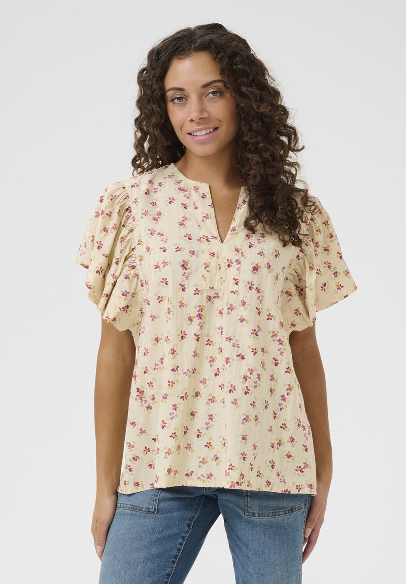 Bluse mit gelben Blumenmotiven, kurzen, gerafften Ärmeln, einem V-Ausschnitt und einem leichten, strukturierten Stoff, verziert mit kleinen rosa und lila Blumen.