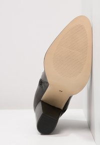 Onderkant van een zwarte leren enkellaars met een blokhak, beige gestructureerde zool en maat nummer 37 zichtbaar.