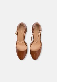 Brune patenterte lær slingback-sko med spiss tå og åpne sider, med detaljer i gulltone og en glatt innside.