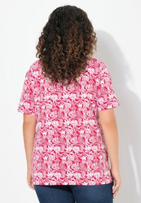 Červený top s květinovým vzorem a krátkým rukávem s bílými detaily, vyrobený z lehkého materiálu, má volný střih a kulatý výstřih.