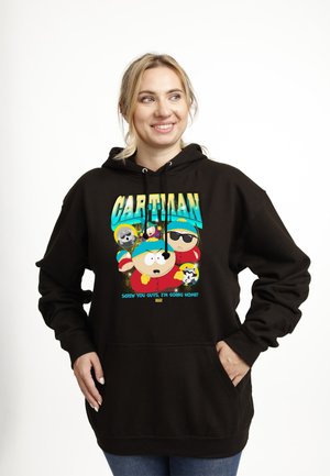 Donna che sorride e guarda a destra, indossa una felpa nera con cappuccio con personaggi colorati di Cartman e la scritta "Screw you guys, I'm going home!"