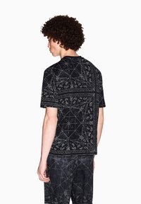 Camicetta nera a maniche corte con un denso motivo geometrico bianco, realizzata in tessuto morbido e con una vestibilità comoda; abbinata a pantaloni coordinati.