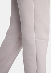 Los pantalones deportivos de color gris claro presentan una textura suave, un ajuste ceñido, bolsillos laterales y un diseño sin costuras a lo largo de las piernas para un aspecto moderno.