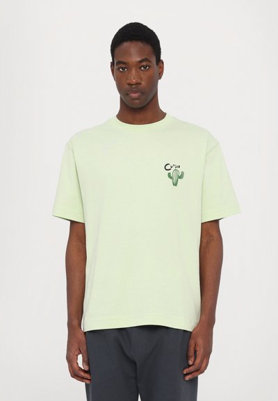 Lys grøn bomulds T-shirt med korte ærmer, rund hals og et kaktus grafisk motiv på venstre bryst. Løs pasform, glat tekstur.