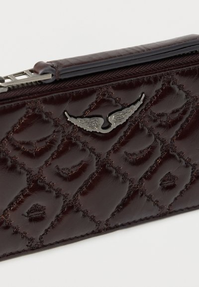 Καφέ δερμάτινο πορτοφόλι με γυαλιστερό φινίρισμα, διακοσμημένο με κεντητό μοτίβο και ασημί λογότυπο με φτερά. Κλείνει με φερμουάρ στην κορυφή.