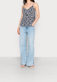 Modrá vzorovaná bezrukávová halenka s volány a řetízkovými ramínky, v kombinaci s širokými džínami s lehkým praním a postranními rozparky. Masivní sandály na podpatku.