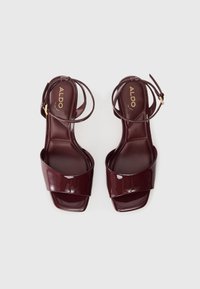 M burgundy lackläder högklackade sandaler med en bred framrem och en tunn vristrem, med en fyrkantig öppen tådesign.