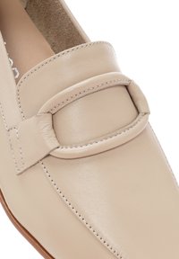 Mocassini in pelle beige con una texture liscia, caratterizzati da una fascia ampia e dettagli di cucitura sottili lungo i bordi. Design con suola piatta.