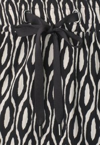 Black and white patterned fabric with a black drawstring tied in a bow through metal eyelets on gathered waistband.
