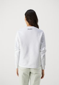 Bílá mikina s dlouhými rukávy a kulatým výstřihem. Na horní části zad je vyšitý logo "KARL LAGERFELD". Bavlněný materiál.