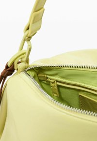 Gelbe Lederhandtasche mit Reißverschluss, ausgestattet mit einem passenden Innenraum und einem verstellbaren Trageriemen mit Metallakzenten.