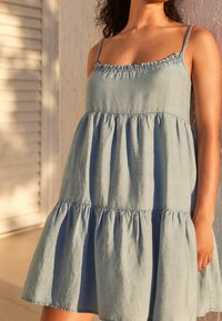 Vaaleansininen puuvillainen kesämekko, jossa on spagettiolkaimet, kerätty kaula-aukko ja kerroksellinen röyhelöhame. Rentoa, löysää istuvuutta.