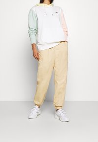 Bílá mikina s kapucí se zelenkavě mátovými a pastelově růžovými rukávy, na přední straně kapsa a černé logo. Volné béžové kalhoty a bílé tenisky doplňují vzhled.