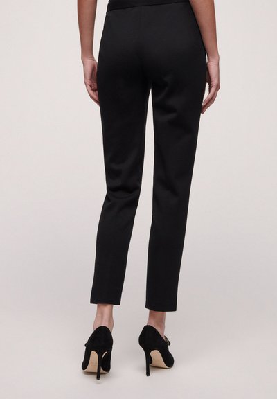 Pantaloni neri su misura con vestibilità slim, caratterizzati da una trama liscia e design alla caviglia, abbinati a scarpe nere con tacco alto.