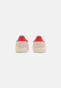 Zapatillas de ante blancas con acentos rojos en el talón. Suela de goma texturizada. Diseño simple y clásico sin patrones ni adornos adicionales.