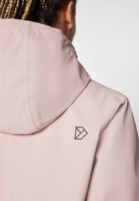 Šviesiai rožinė striukė su gobtuvu ir lygiu tekstūru. Turtinga trikampė logotipo detalė nugaroje ir siuvimo apdaila aplink gobtuvą.