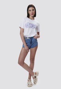 Witte T-shirt met "Do.it" graphic in paars, gecombineerd met denim shorts en beige sandalen met bandjes, die een casual, ontspannen uitstraling benadrukken.