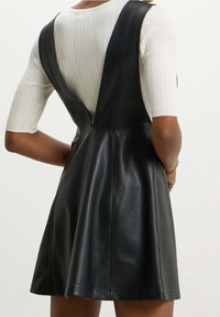 Vestido de cuero negro con falda acampanada, con tirantes anchos y cuerpo ajustado. Textura suave sin patrones visibles.