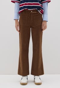 Pantalones acampanados de pana marrón con una textura suave, que cuentan con bolsillos frontales y un cordón, combinados con una camiseta a rayas y zapatillas blancas.