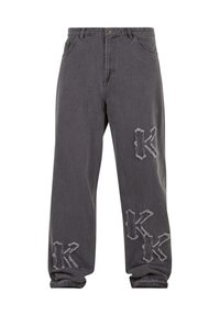 Vaqueros grises de corte ancho con parches bordados desgastados con la letra "K" en el muslo izquierdo, la rodilla derecha y la zona del tobillo izquierdo.