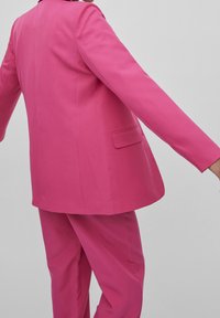 Fuchsia blazer med långa ärmar och en bakficka, ihop med matchande smalna byxor, slätt tyg med en strukturerad passform.