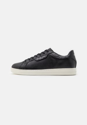Baskets basses en cuir noir texturé avec lacets noirs et semelle blanche, logo latéral et patte de talon lisse.