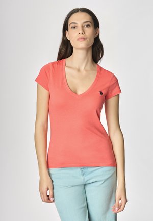 T-shirt a V in corallo con maniche corte, realizzato in tessuto morbido; presenta un piccolo logo scuro sul petto sinistro. Abbinato a pantaloni blu chiaro.