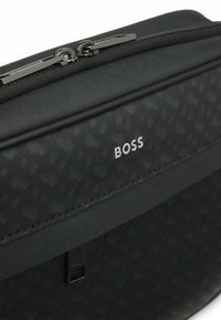 Borsa in tessuto nero con motivo testurizzato, hardware argentato, chiusura con zip superiore, con logo "BOSS" stampato in bianco.