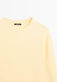 Light yellow sweater made from soft fabric, featuring a classic round neckline and ribbed edges, with minimalistic branding on the inside.