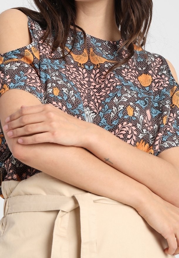Bluse mit Floral-Muster und kalten Schultern in den Farben Orange, Blau und Pink, aus leichtem Stoff gefertigt. Sie hat einen runden Ausschnitt.